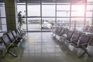 Airplane, view from airport terminal. Modern airport terminal with black leather seats on a sunny...