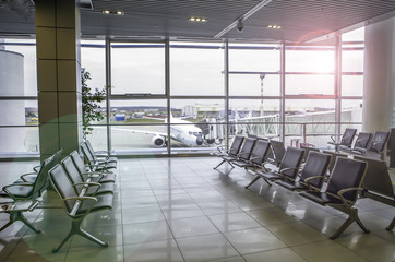Airplane, view from airport terminal. Modern airport terminal with black leather seats on a sunny...