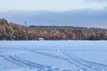 Obraz premium Snowmobile trail on a snowy frozen lake against the forest.