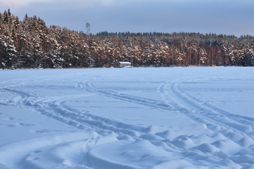 Snowmobile trail on a snowy frozen lake against the forest.