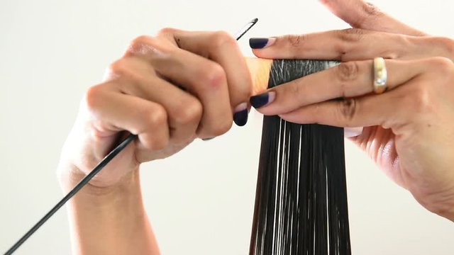 Close up of the hands of a female hairstylist doing a perm rolling the clients hair onto fine rollers or curlers for a curly or wavy effect