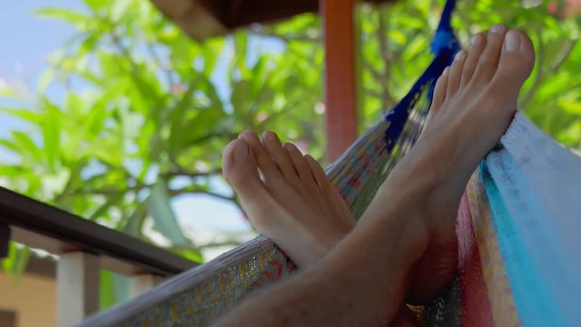 Swinging bare man feets in a hammock on terrace. Vacation on Koh Tao Tanote Bay, Thailand