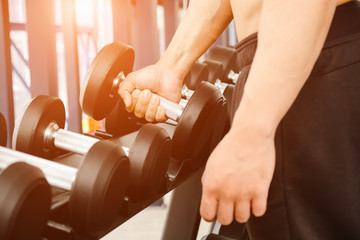 close up of man holding rows of dumbbells in the gym.Gym equipment and sport concept.