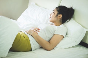 Asian young woman suffering from abdominal pain while on bed at home