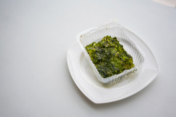 Last piece of Korean fried seaweed in plastic container of packing on white plate isolated on white table.