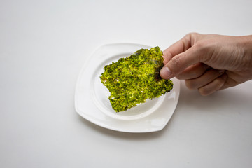 Hand picking Korean fried seaweed sheet over white plate on white background.