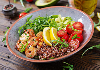 Delicious healthy Buddha bowl with shrimps, tomato, avocado, quinoa, lemon and arugula on the wooden table. Healthy food.