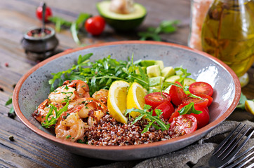 Delicious healthy Buddha bowl with shrimps, tomato, avocado, quinoa, lemon and arugula on the wooden table. Healthy food.