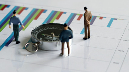 Fototapeta premium appearance from behind of compass and three miniature men on the chart