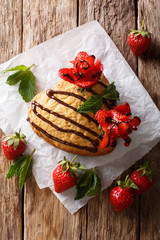 Delicious sponge cake in the shape of heart, decorated with chocolate and strawberry roses close-up. Vertical top view