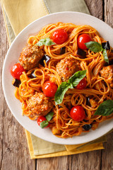 Spaghetti with meat balls, vegetables in a tomato sauce close-up on a plate on a table. Vertical top view, rustic