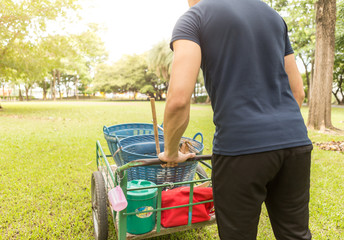 Young man work to cleaning park with a garden cart, broom, rake, watering can and buckets in garden or park.