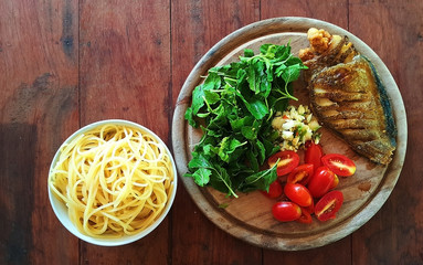 A set of ingredients for cooking spaghetti with dry crispy fish and basil  : spaghetti, tomatoes, garlic, pepper, chilli, dry crispy fish, basil, on wooden table