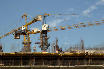 building, people in helmets, tower cranes against the sky