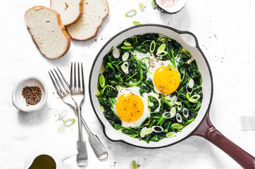 Green shakshuka. Fried eggs with fresh spinach, ramson, leek in a cast iron skillet on a white...