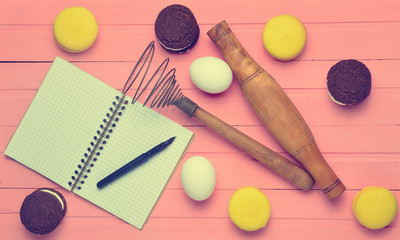 The process of making chocolate cookies, macaroons, ingredients on a pink wooden background. Eggs, rolling pin, corolla, recipe notebook with a pen. Top view.
