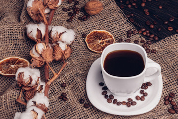 Grains of coffee next to a cup of coffee with cotton on the sack