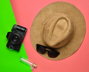 Creative flat lay fashion style with camera, sunglasses, bottle of perfume and felt hat on pastel...