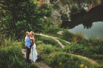 Beautiful and lovely newlyweds stand on a cliff, against the background of rocks and river. Wedding portrait of a stylish bride and a cute bride.