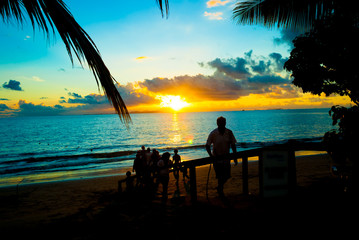 People family friend enjoying beautiful quiet calm sunset at a sandy beach with calm wave water and blue orange sky at an island