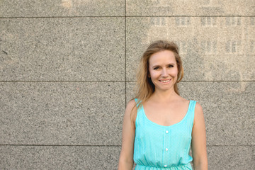 Waist up emotional portrait of a blonde woman in a blue sundress near a granite textured wall with a reflective surface