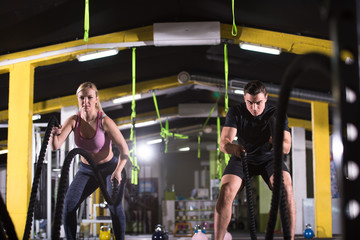 sports couple doing battle ropes cross fitness exercise