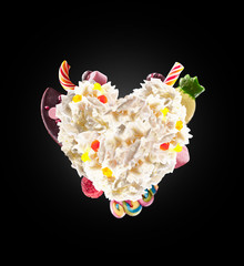 Heart form from whipped cream with sweets, jellies, heart front view. Crazy freakshake food trend. Front view of whipped heart of cream, full of berry and jelly sweets, chocolate candy. Colored