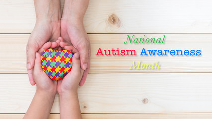 Obraz premium National Autism Awareness month concept with puzzle or jigsaw pattern on heart with autistic child's hands supported by nursing family caregiver