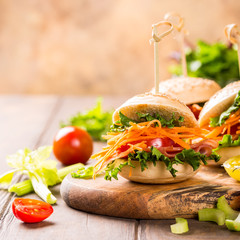 Homemade mini burgers with ham, tomato, carrot, fresh salad served on wooden board. Healthy junk food concept with copy space.