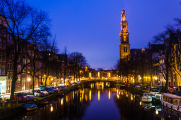 Fototapeta premium Sunrise on a canal with old historical church on the horizon in Amsterdam water Holland bridge for summer holiday vacation family couple and friends
