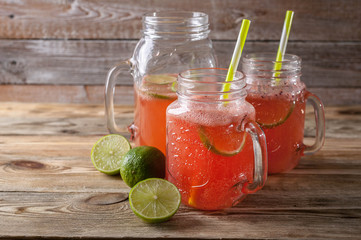 Homemade lemonade with strawberry slices and lime slices in glass jars on a wooden table