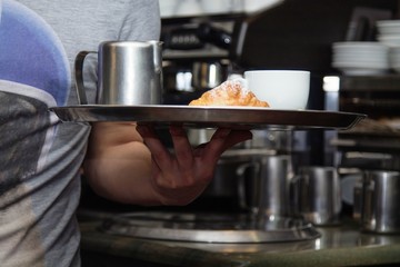 waiter serving coffee and croissant on tray