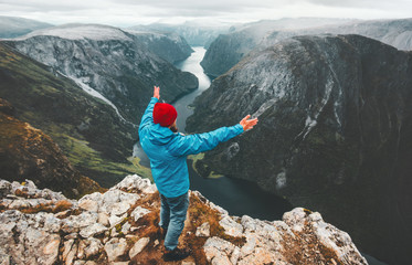 Brave traveler man raised hands traveling in Norway standing on cliff mountain active lifestyle...