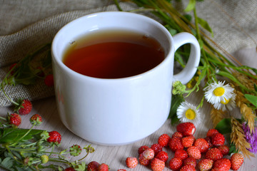 Cup of tea, flowers and wild strawberries on the table