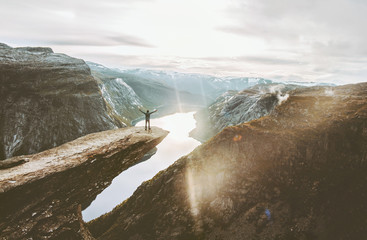 Man on Trolltunga cliff edge happy raised hands traveling in Norway adventure lifestyle extreme vacations outdoor sunset mountains landscape aerial view.