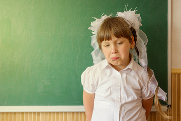 The girl is standing near the chalkboard, sad not knowing the answer.