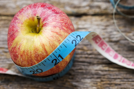 Close-up of red apple wrapped with measurement tape on wooden table