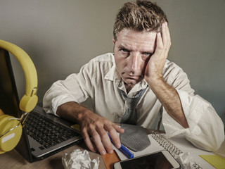 attractive sad and desperate man in lose necktie looking messy and depressed working at laptop...