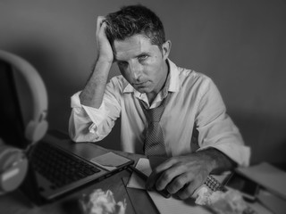 attractive sad and desperate man in lose necktie looking messy and depressed working at laptop...