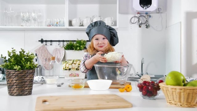 Preschool girl baker on kitchen mixes and tastes the dough in a bowl