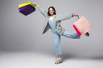 Full length portrait of a happy pretty girl holding shopping bags while running and looking at camera isolated over gray background