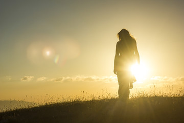 silhouete of girl in dress standing on grass in sunset mountains