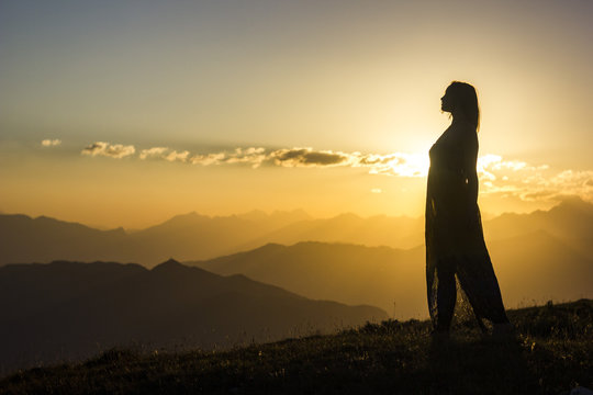 silhouete of girl in dress standing on grass in sunset mountains