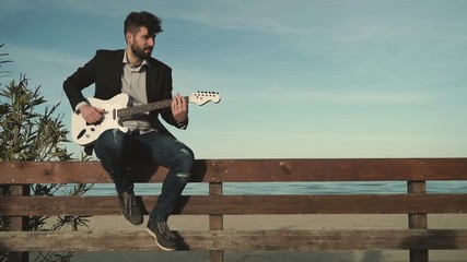 Young male guitarist playing a beautiful white electric guitar near the sea, people passing by on bikes. - Powered by Adobe