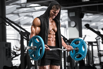 Muscular man working out in gym doing exercises with barbell for biceps, strong male naked torso abs