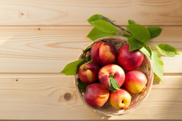 fresh nectarine with leaves  are in a wicker plate on a light wooden table in the sun. close-up