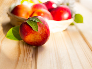 fresh nectarine with leaves  are in a wicker plate on a light wooden table in the sun.  close-up