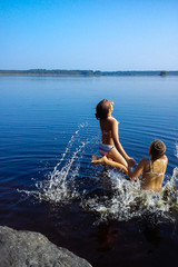 Kids jump into water, girls swim in the forest lake. Children having fun on a summer vacation, splashing water.