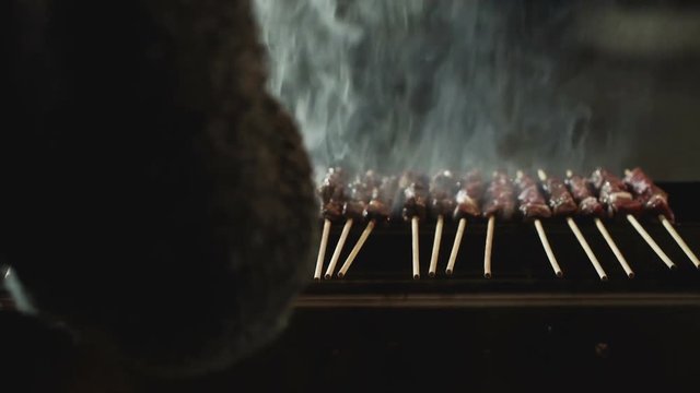 Girl gently turning arrosticini on the grate to cook them properly.