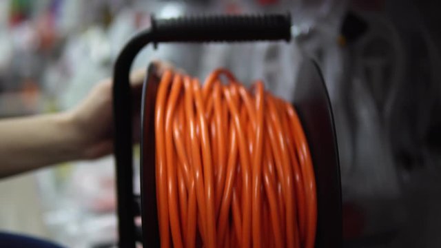 A young woman in a blue checkered shirt chooses and buys an extension lead in the supermarket in the building materials department.